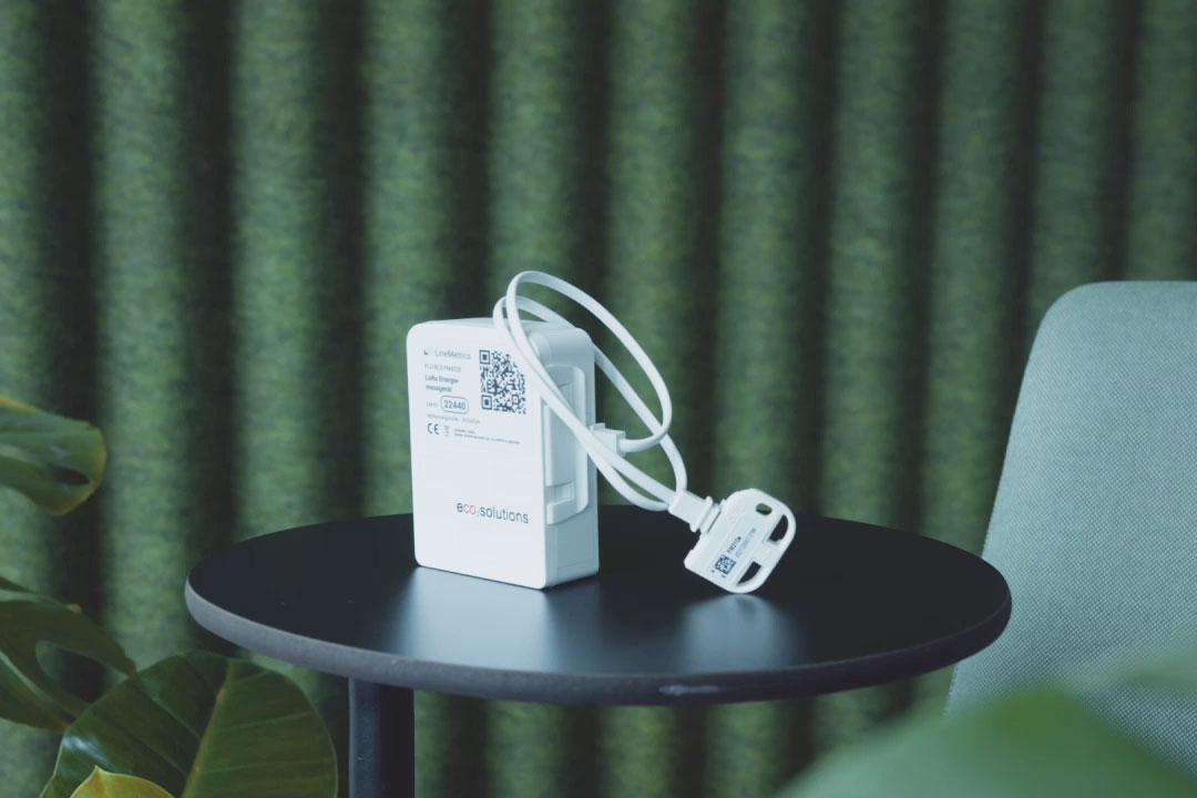 Image of an eco2state sensor with cable and plug standing on a round table against a green background.