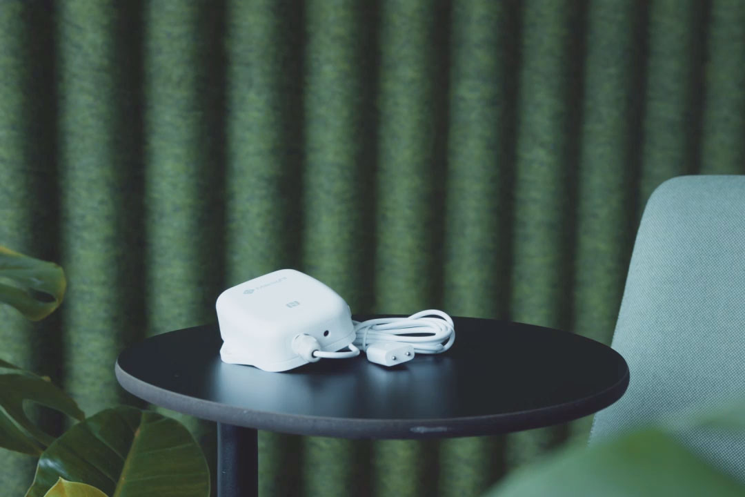 Image of an eco2state sensor with cable and plug standing on a round table against a green background.