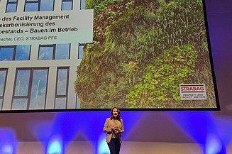 Baukongress Aachen 2024 Bild von einer Frau, die auf einer Bühne eine Präsentation hält