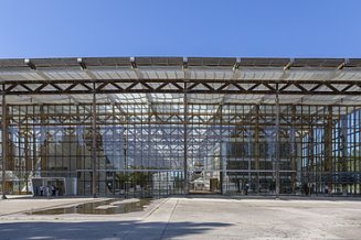 Foto von einem großen Gebäude aus Glas und Stahlträgern mit einem großen Vorplatz aus Beton
