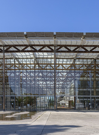 Foto von einem großen Gebäude aus Glas und Stahlträgern mit einem großen Vorplatz aus Beton