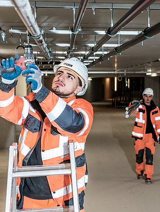 Photo of a man in protective clothing screwing a pipe to a cellar ceiling