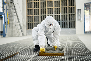 Eine Person in Schutzanzug und Handschuhen reinigt ein Gitter