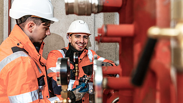 Lehrling an einer technischen Anlage lacht in die Kamera