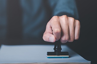 Image of a hand making a certification and pressing a stamp on a sheet of paper