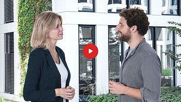 Vorschaubild Yotube Video: eine Frau und ein Mann stehen vor einem begrünten Gebäude und sich gegenüber