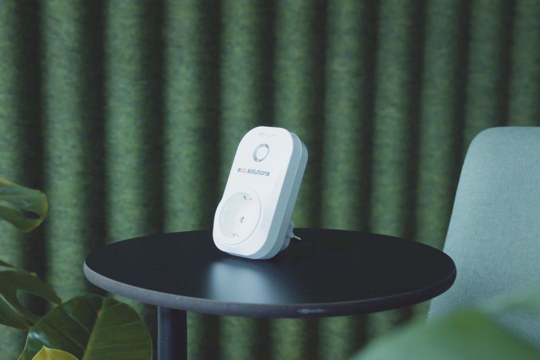 Bild von einem Steckdosenadapter inklusive eco2state Sensor, welcher auf einem runden Tisch vor grünem Hintergrund steht.