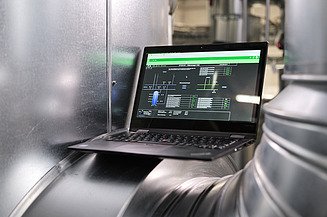 Ein Laptop mit Steuerungsprogramm steht auf einem großen Metallrohr in einer industriellen Umgebung