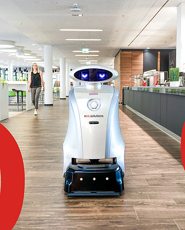 Obrázek úklidového robota v jídelně pro automatizovaný a hygienický úklid. Vidět jsou i velké červené displeje C, O a 2.