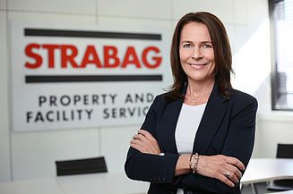 Foto von einer Frau im Businesslook vor einer Wand, auf der STRABAG Property and Facility Services steht