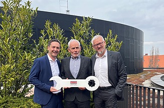 Photo of three men on a balcony holding a large key