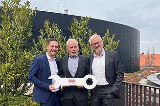 Photo of three men on a balcony holding a large key