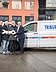 Picture of four persons holding a big key in front of a building and two cars