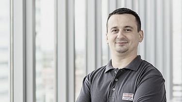 STRABAG PFS Mitarbeiter steht mit verschränkten Armen vor einer modernen Fensterfront