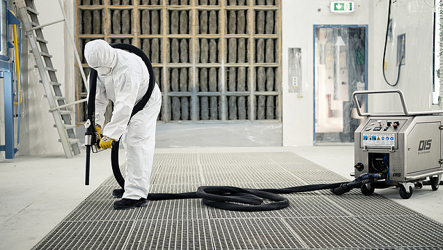 Person in Schutzkleidung reinigt mit einem Industrieschlauch in einem Reinraum oder kontrollierten Bereich.
