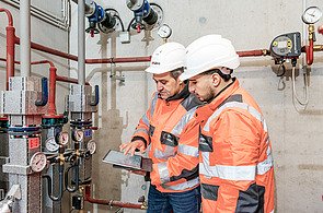 STRABAG PFS Lohr GmbH Foto von zwei Personen in Schutzkleidung, die vor einer technischen Anlage auf ein Tablet schauen