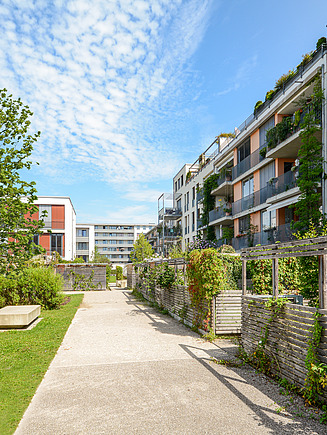 Modern multi-storey residential building with colorful facades and windows, surrounded by a wooden fence, under a clear sky.