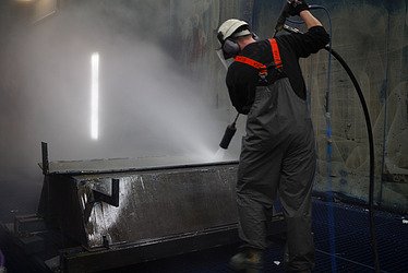 Bild von einer Person, die Industrieservices durchführt und eine Wanne mit Strahlverfahren reinigt