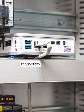 Bild von einer weißen angeschlossenen Technikbox in einem Schaltschrank neben weiteren technischen Geräten