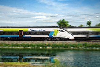 Picture of a train passing another train quickly, reflected in the water in the foreground