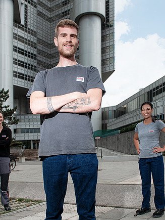 Fotografie čtyř zaměstnanců před věžákem, kteří se usmívají do kamery