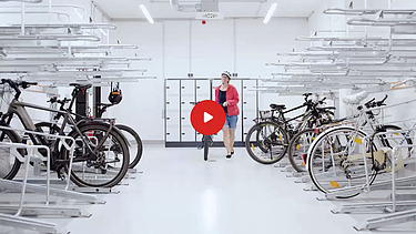 Preview image of a video: a woman pushes her bicycle to a metal bracket in a bicycle cellar