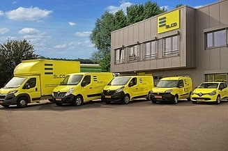 With the acquisition of ELCO, STRABAG PFS is expanding into Luxembourg. Photo of a fleet of yellow vehicles in front of a building