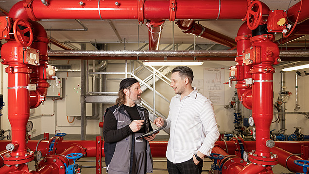 Foto von einem Objektbetreuer und einem Techniker, die sich in einem Technikraum ein Tablet anschauen