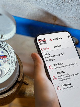 Image of a smartphone with the STRABAGmeter app open in the foreground and the corresponding analog meter in the background.