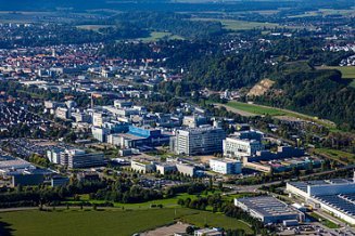 Luftaufnahme einer Stadt und eines Gebäudekomplexes, umgeben von Grünanlagen und Wald