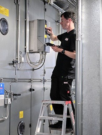 Photo of a person standing on a stepladder and carrying out a test on an installation