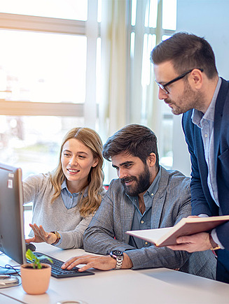 Two men and a woman look at content on a PC screen together.