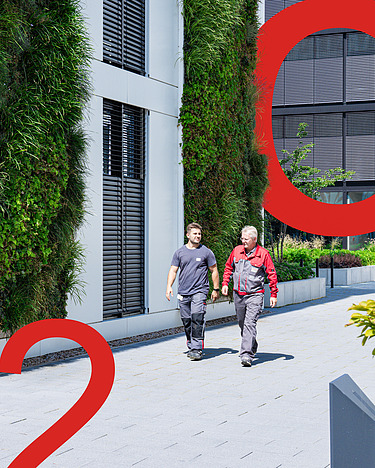 Picture of two men walking next to a vertically planted building, in front of which are large red displays of C, O and 2.