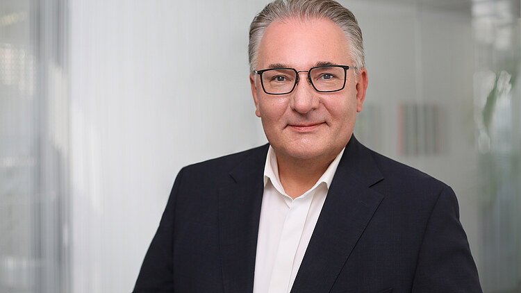 Generální ředitel Marko Bohm - podnikatel v tmavém obleku a pruhované kravatě se usmívá před neutrálním pozadím, profesionální obchodní portrét.