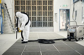 Eine Person in Schutzkleidung bedient einen großen Industrieschlauch in einer industriellen Anlage.