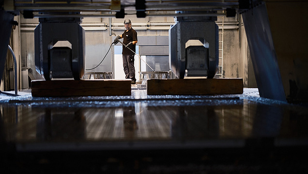 Ein Arbeiter in Schutzkleidung reinigt mit einem Hochdruckreiniger den Bodenbereich in einer Fabrikumgebung