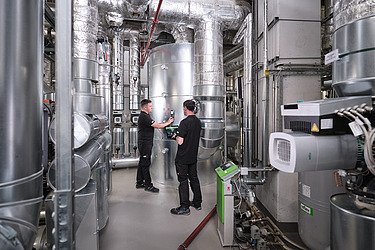 Foto von Mitarbeitenden in einem Technikraum mit Rohren, an denen sie arbeiten