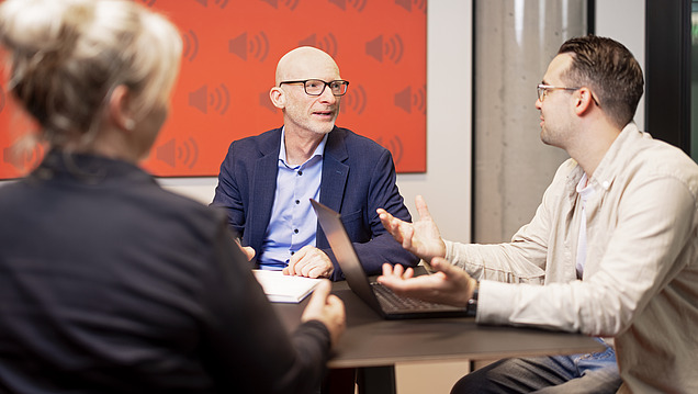 A group of people in a seminar, with one person smiling and raising their hand to ask a question.