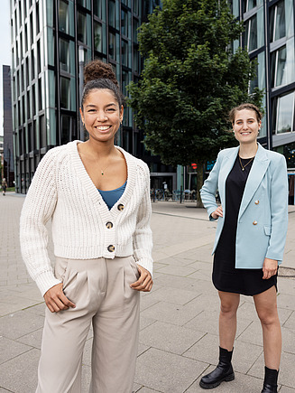 Fotografie čtyř zaměstnanců před věžákem, kteří se usmívají do kamery