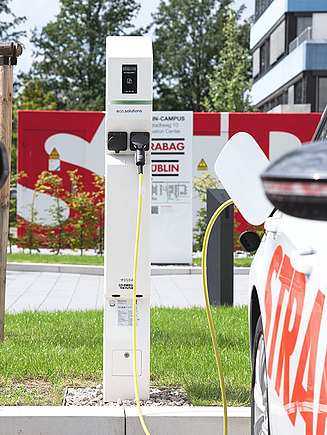Bild von zwei geparkten STRABAG Autos, in der Mitte eine eco2mobility E-Ladestation, welche durch ein Kabel mit einem Auto verbunden ist