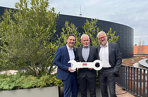 Photo of three men on a balcony holding a large key
