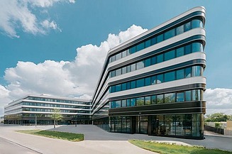 Bild von einem 4. stöckigen Gebäude inklusive Glasfronten vor einem blauen Himmel