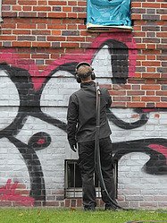 Obrázek osoby odstraňující graffiti ze zdi