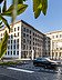 Bild von einem historischen Gebäude, die Vorfahrt ist beflaggt, auf der Straße ist ein vorbeifahrendes Auto zu sehen