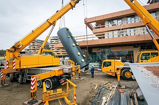 Eine technische Anlage wird mit Kränen unter ein Gebäude abgelassen.