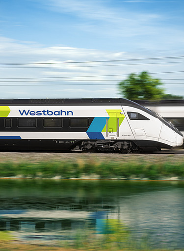 Moderner Westbahn-Zug in Weiß mit blau‑grünen Akzenten fährt mit hoher Geschwindigkeit an einer grünen Landschaft vorbei.