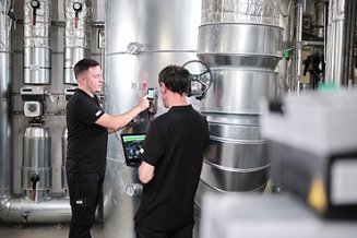 Picture of two men at a piece of equipment, carrying out checks using a measuring device and a laptop