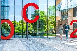 eco2consult Foto eines Glasgebäudes mit zwei vorbeigehenden Personen und großen roten Buchstaben O, C, 2