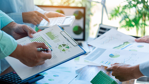 Image of several people evaluating charts and reports with green graphs and a calculator;