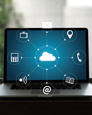 Ein Laptop auf einem Tisch zeigt ein Netzwerkdiagramm mit einer zentralen Cloud, die mit verschiedenen digitalen Symbolen verbunden ist.